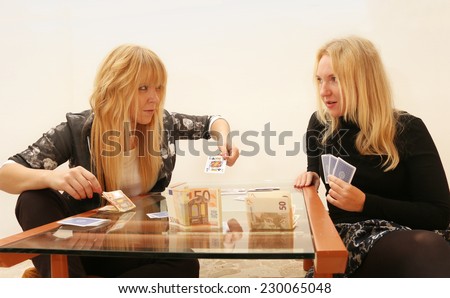2 girl friends play cards at home betting for money, one plays the right trump card and wins.  friendship and competition concept