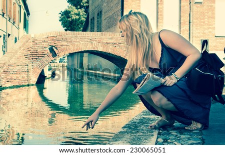 Young female tourist in an ancient romantic southern European destination, sitting by the  quiet water canals in the idyllic Comacchio town in Italy. vintage style filtered image