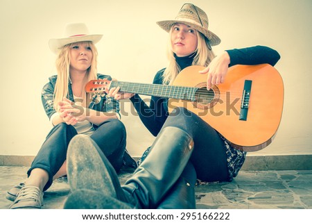 best friends play guitar 2 girls sitting on the floor wearing hats playing guitar and making music vintage look filter and faded colors applied
