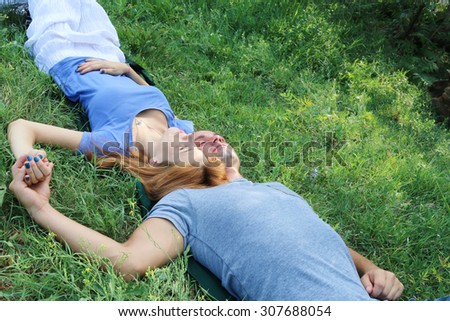 young beautiful couple in love, hand in hand, lying on the green grass in a park closing eyes and dreaming. concept of true love tenderness and future hopes.