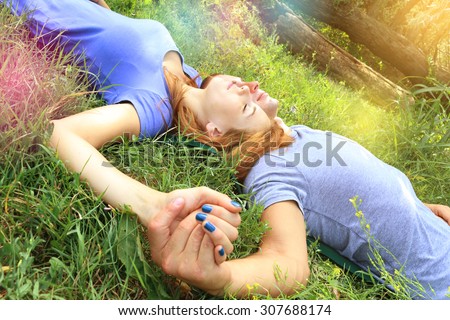 young attractive couple in love, hand in hand, lying on the green grass in a park closing eyes and dreaming. concept of true love tenderness and future hopes. sunburst and lens flare effects added.