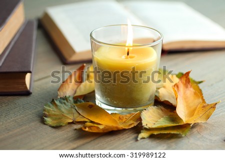 candle with leaves and books on wooden background