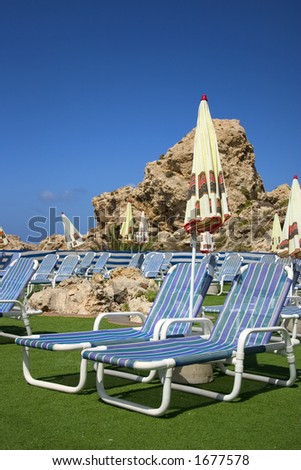 An empty poolside resort with focus on the two deckchairs in foreground