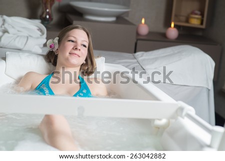 Young pretty woman with flower in the hair taking a bath at the hotel spa
