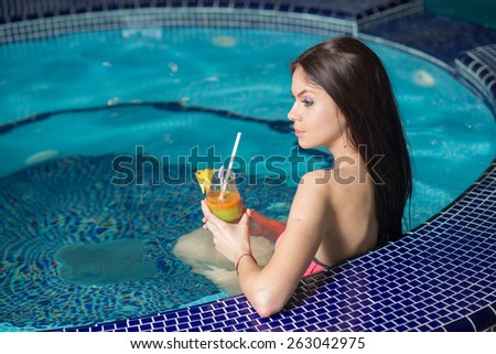 Young woman with cocktail sitting in jacuzzi in the swimming pool at the hotel spa