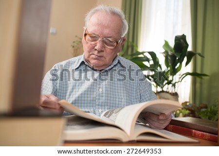 Old man in glasses reading a books in the room. Close portrait
