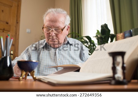 Old man in glasses writing from the books in the room. Close portrait