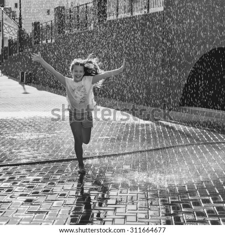 Happy beautiful girl running through the spray of water. Black and white photo