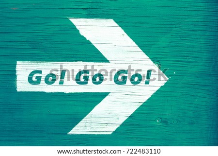'Go! Go! Go!' text written on a white directional arrow pointing towards right manually painted on a green blueish wooden signboard background. Photo framed horizontally. 商業照片 © 