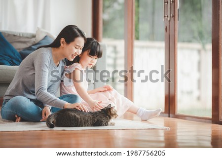 Happy Asian family mother and daughter palying with cat at home in living room. Focused on mother