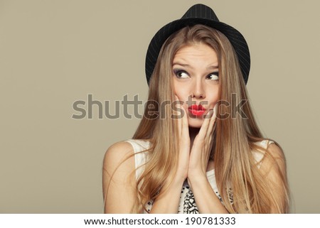 Surprised happy young woman looking up in excitement. Fashion girl in hat. isolated on beige background