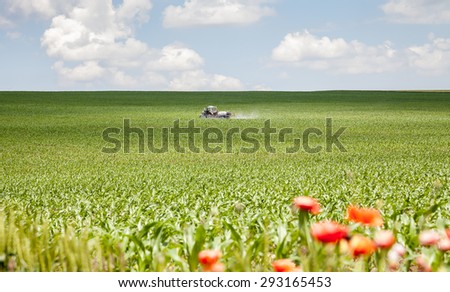 Landscape with tractor sprayer carried chemical treatment of crops against pests poppies in the foreground