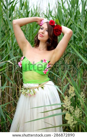 Female model from Poland posing near the lake, surrounded by reeds. Woman wearing flowers\' wreath, colorful dress. Chestnut hair color.