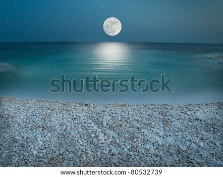 Pebble beach in the the night wit clear sky with stars, lit by the full Moon just above horizon