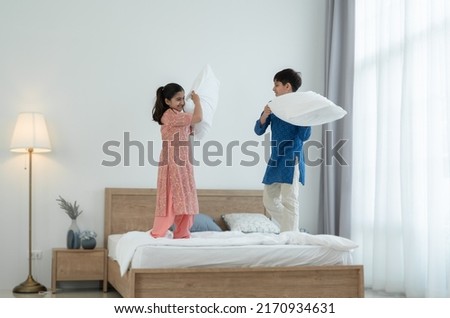 Two happy Indian brother and sister in traditional clothing standing on bed, playing pillow fight, having fun together at home. Playful kids, Siblings relationship concept Foto stock © 