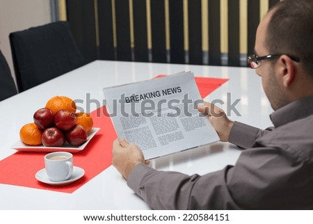 Man reading breaking news article in the newspaper at home.