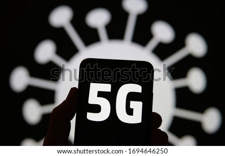 5G radiation in a shape of COVID-19. 5G letters on smartphone silhouette hold in a hand and coronavirus image on the background. Real photo, not a a montage. 5G conspiracy fake news, arson concept. 