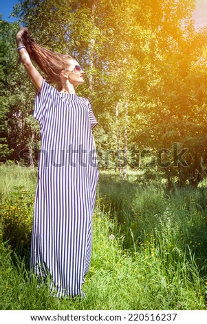 Girl holds himself for loose hair standing in a dress on nature