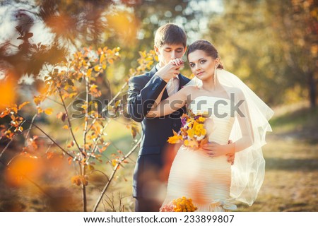 Wedding photography in autumn park where young groom kissing his hand gently bride in her wedding dress