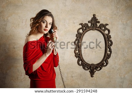 Portrait of a beautiful girl in the red dress, she is holding handset of old phone