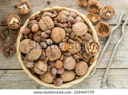 Hazelnuts, walnuts and pine nuts in a wicker basket on a wooden table