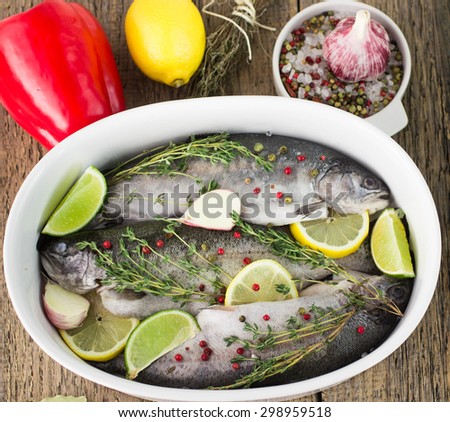 Three raw rainbow trout in a baking dish with lemon, lime, garlic, thyme and pink pepper. Shallow depth of field