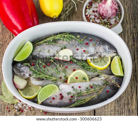 Three raw rainbow trout in a baking dish with lemon, lime, garlic, thyme and pink pepper. Shallow depth of field