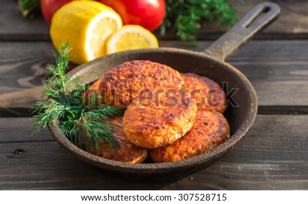 salmon fishcakes in a cast iron skillet, tomatoes and lemon on a dark table. Selective focus
