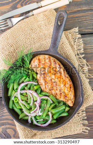 Grilled chicken breast and green beans in a cast iron skillet on the table. Selective focus