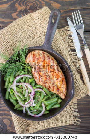 Grilled chicken breast and green beans in a cast iron skillet on the table. Selective focus