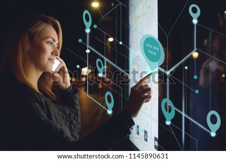 Young woman calling via mobile phone while checking public transport schedule on electronic bulletin board, female touching digital display of modern bus station for choose location. Infographics map 商業照片 © 