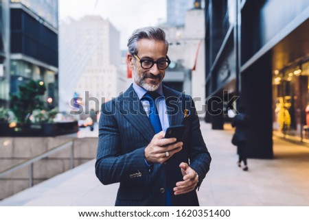 Foto Bild Gut gekleideter Mann beim Surfen auf dem Smartphone in der Stadt