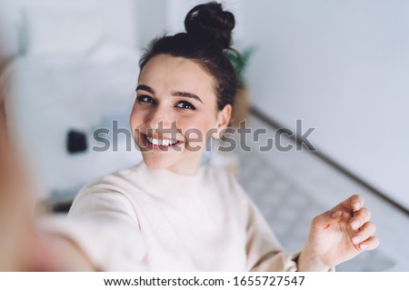 Good mood lady with expansive smile enjoying started weekends and taking selfie on mobile phone on blurred background