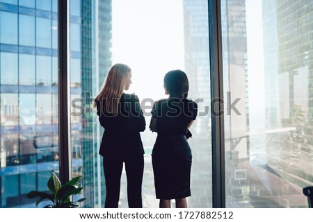 Back view of female colleagues in formal wear standing near window and communicating about cooperation in business center, confident women together planning future success of brainstorming ストックフォト © 