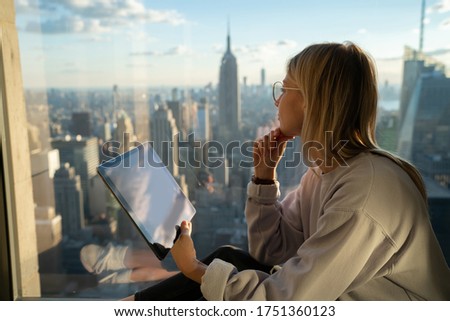 Thoughtful female digital nomad with modern touch pad looking in panoramic window while creation social content for sharing to web blog, millennial hipster girl with gadget for online communication Imagine de stoc © 