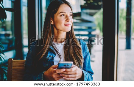 Attractive female blogger with modern smartphone gadget in hands thoughtful looking away and dreaming, youthful Caucasian blogger holding cellphone pondering thinking on idea for social publication