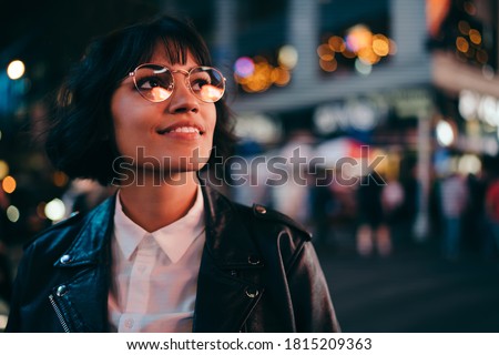 Carefree brunette young woman with short haircut in stylish eyewear for eyes protection fascinated with New York urbanity in Manhattan,youthful female in leather jacket enjoying metropolitan nightlife