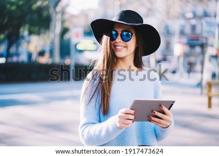 Trendy dressed hipster girl in stylish sunglasses and hat holding modern touch pad standing at city street and smiling,happy female blogger with digital tablet or ebook enjoying sunny day on vacations Imagine de stoc © 