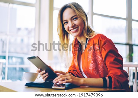 Portrait of cheerful hipster girl with perfect smile on face using digital tablet and posing in coffee shop, joyful Caucasian web blogger with modern touch pad technology enjoying leisure in cafe Imagine de stoc © 