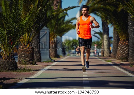 Muscular athletic man in the bright sportswear running on the jogging track