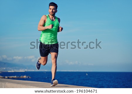 Attractive strong athlete running along the sea at evening