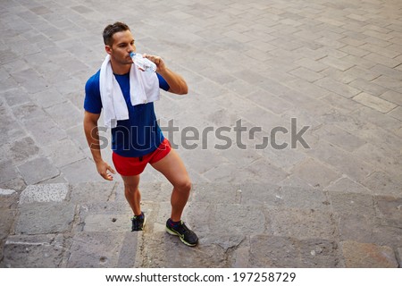 Handsome muscular runner after a long run in the old town resting and drinking water