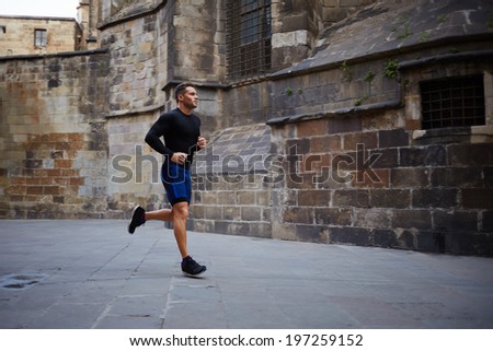 Strong attractive athlete runs through the city on morning jog