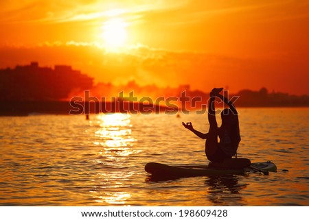 Silhouette of the paddle board yoga training accompanied by a stunning sunset reflected on the sea, yoga meditation on the beach