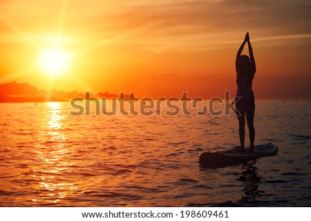 Silhouette of standup paddle board yoga performed by beautiful girl on the bright sunset background,  evening sup yoga meditation