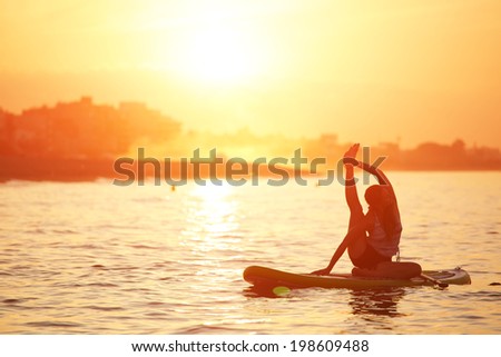 Beautiful woman engage paddle surf yoga at the amazing sunset over the sea, spiritual yoga meditation on the beach, silhouette