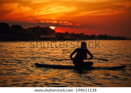 Beautiful girl doing yoga meditation on the paddle surf board accompanied by a stunning sunset