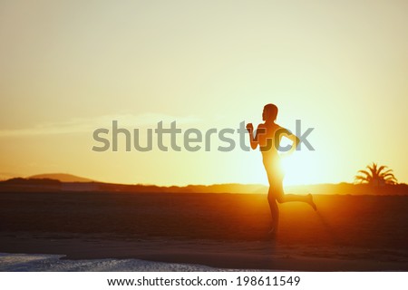 Silhouette of female runner through the rays of the sun running along the sea