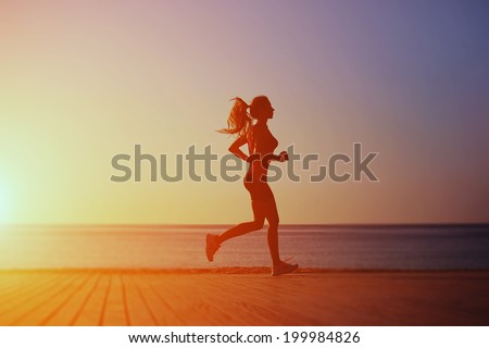 Bright silhouette of athletic female runner with a beautiful figure runs on the wooden pier on the sea and sky background, morning jog on the beach