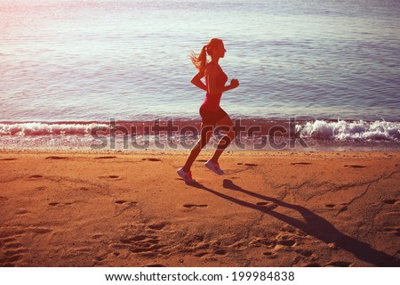 Bright silhouette of attractive female runner with a beautiful strong figure running on the beach on the sea background